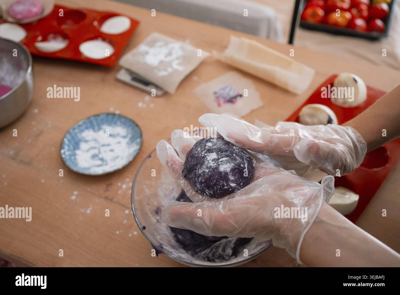 Mains portant des gants façonnant la pâte mochi violette en boules rondes, préparant un dessert sucré japonais fait à la main dans une cuisine maison, saupoudrer de farine Banque D'Images