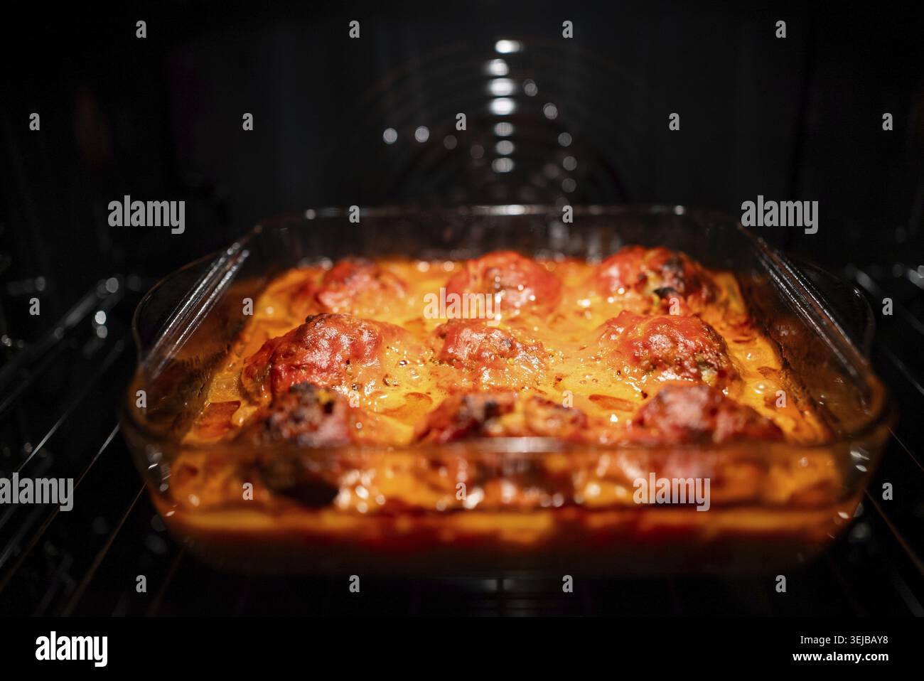 Boulettes de viande maison mijotant dans une sauce tomate vibrante dans une casserole en verre clair, rôtissant dans un four chaud, présentant une délicieuse culina Banque D'Images