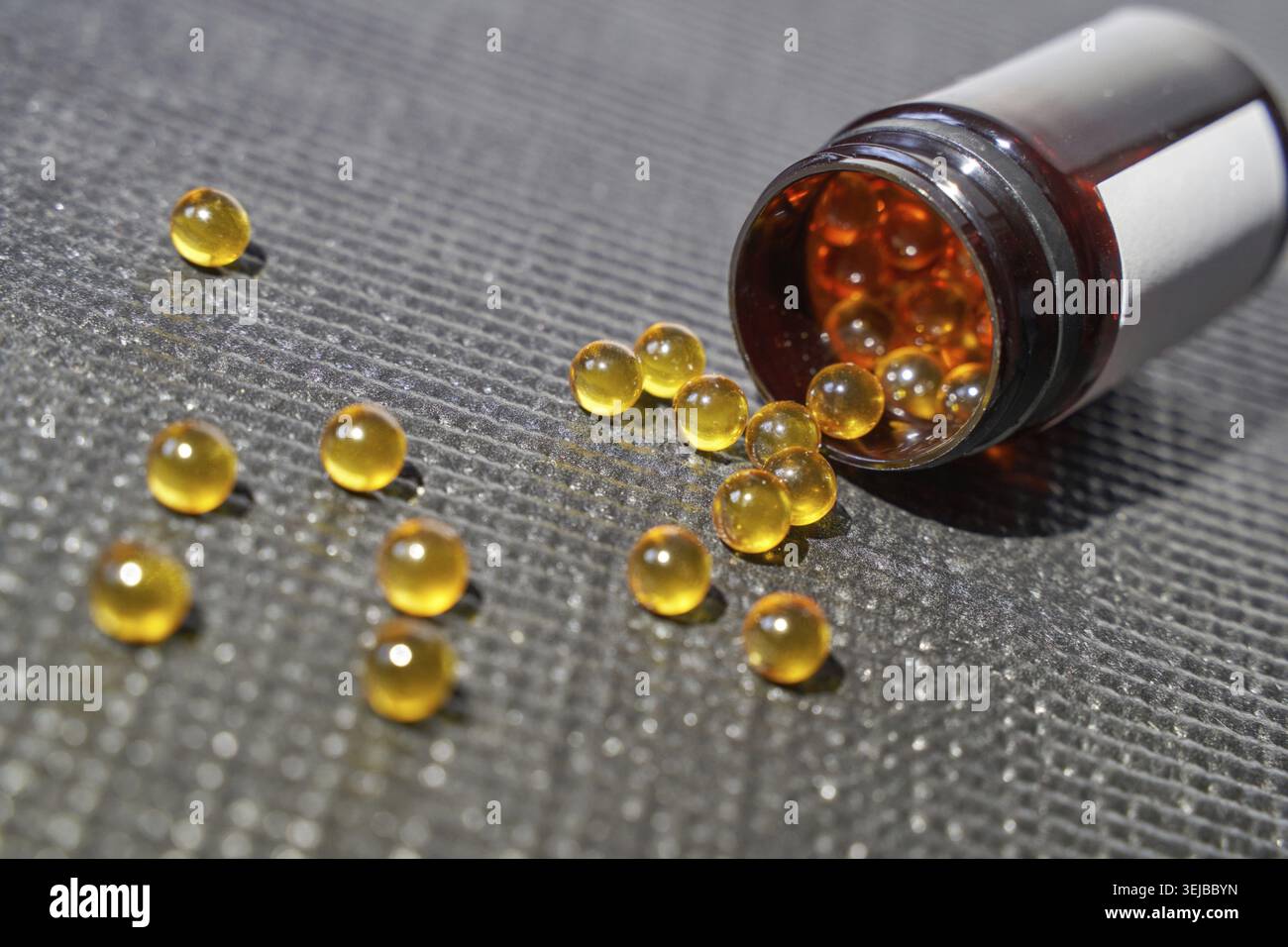 Capsules ambrées renversées de bouteille brune sur la surface grise - concept de suppléments vitaminiques Banque D'Images
