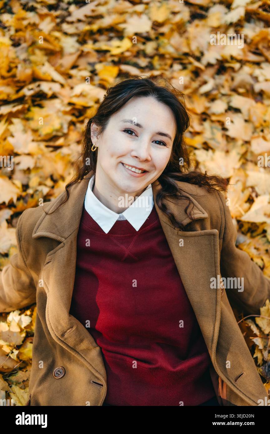 Femme souriante se trouve sur le sol couvert de feuilles d'automne regardant vers le haut. Détox numérique employé de bureau, concept de congé personnel, gestion du stress pour Banque D'Images