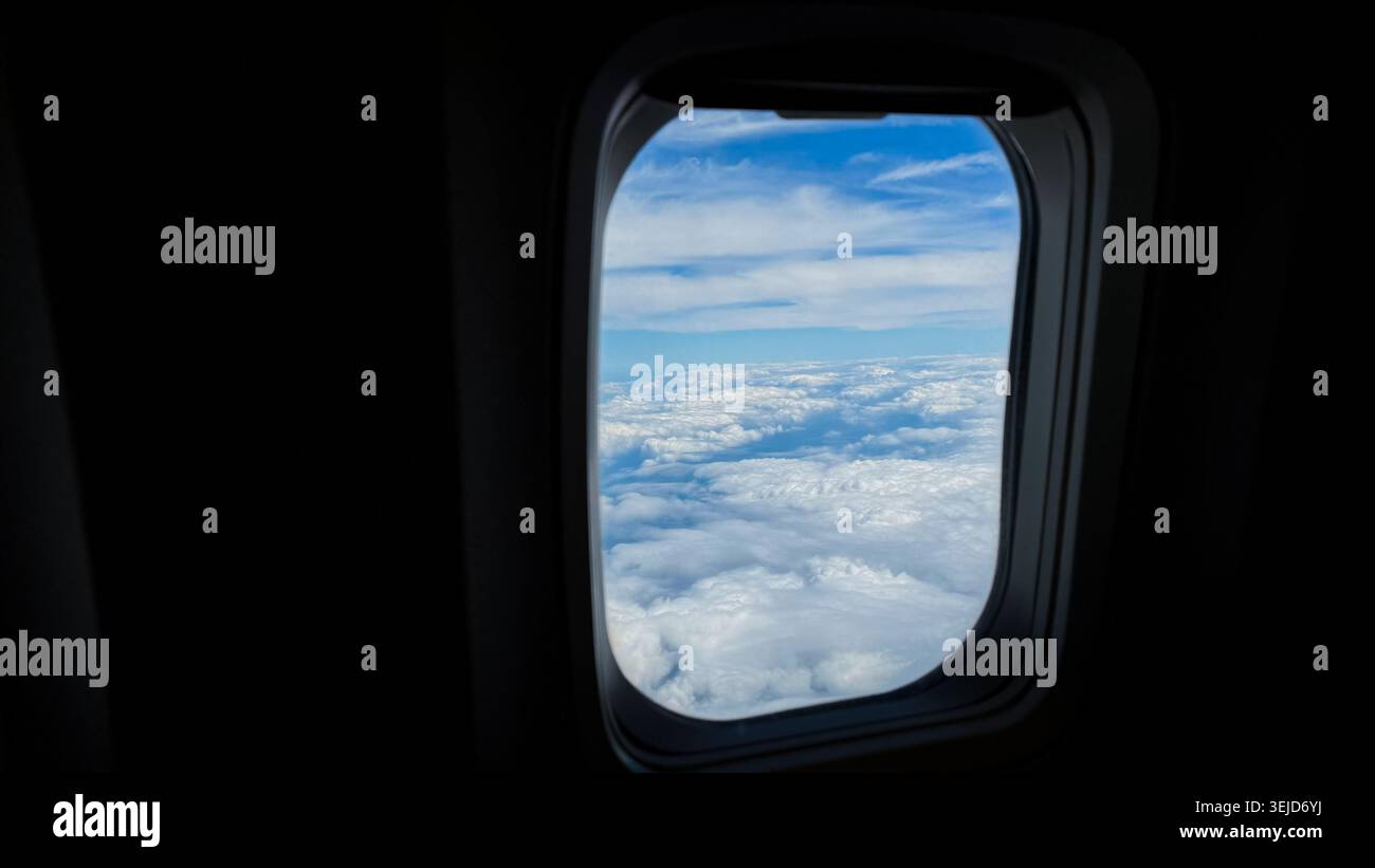 Vue de la fenêtre de l'avion montrant des nuages blancs pelucheux et un ciel bleu, avec un horizon clair visible au-delà du cadre de l'avion Banque D'Images