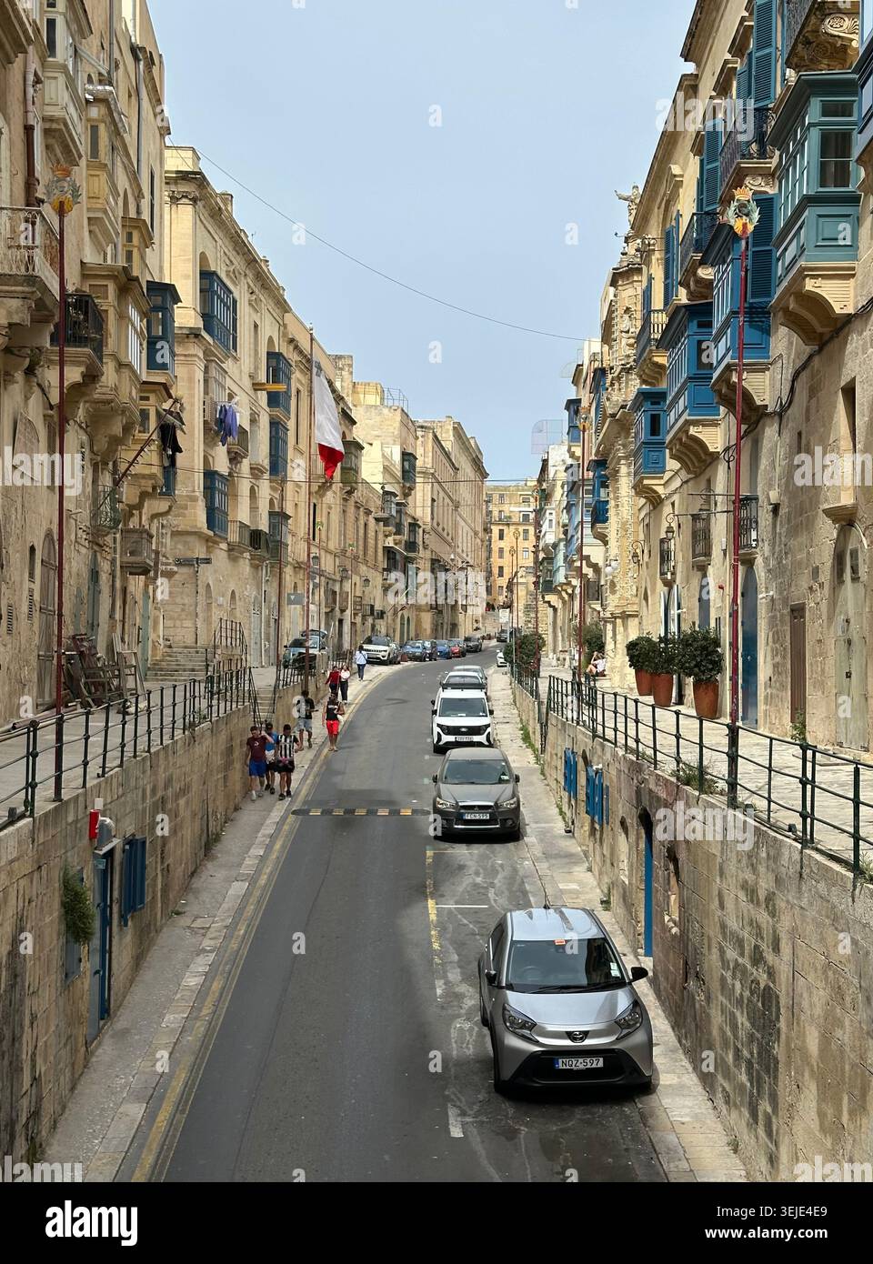 Rue étroite de la Valette, Malte, bordée de bâtiments historiques en calcaire avec balcons en bois coloré. Plusieurs véhicules sont stationnés le long de la R. Banque D'Images