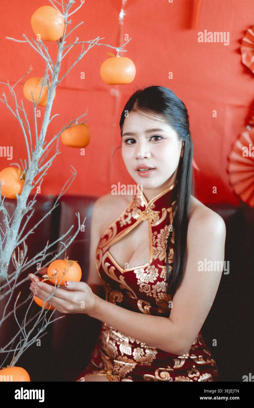 Heureuse femme asiatique dans le cheongsam rouge traditionnel célébrant le nouvel an chinois. beau portrait de femelle tenant orange chanceux contre backgro festif Banque D'Images