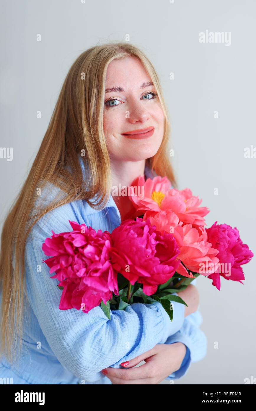 Femme heureuse embrassant des fleurs colorées dans un studio lumineux, beauté et concept de soins personnels avec un maquillage naturel et des couleurs douces. Banque D'Images