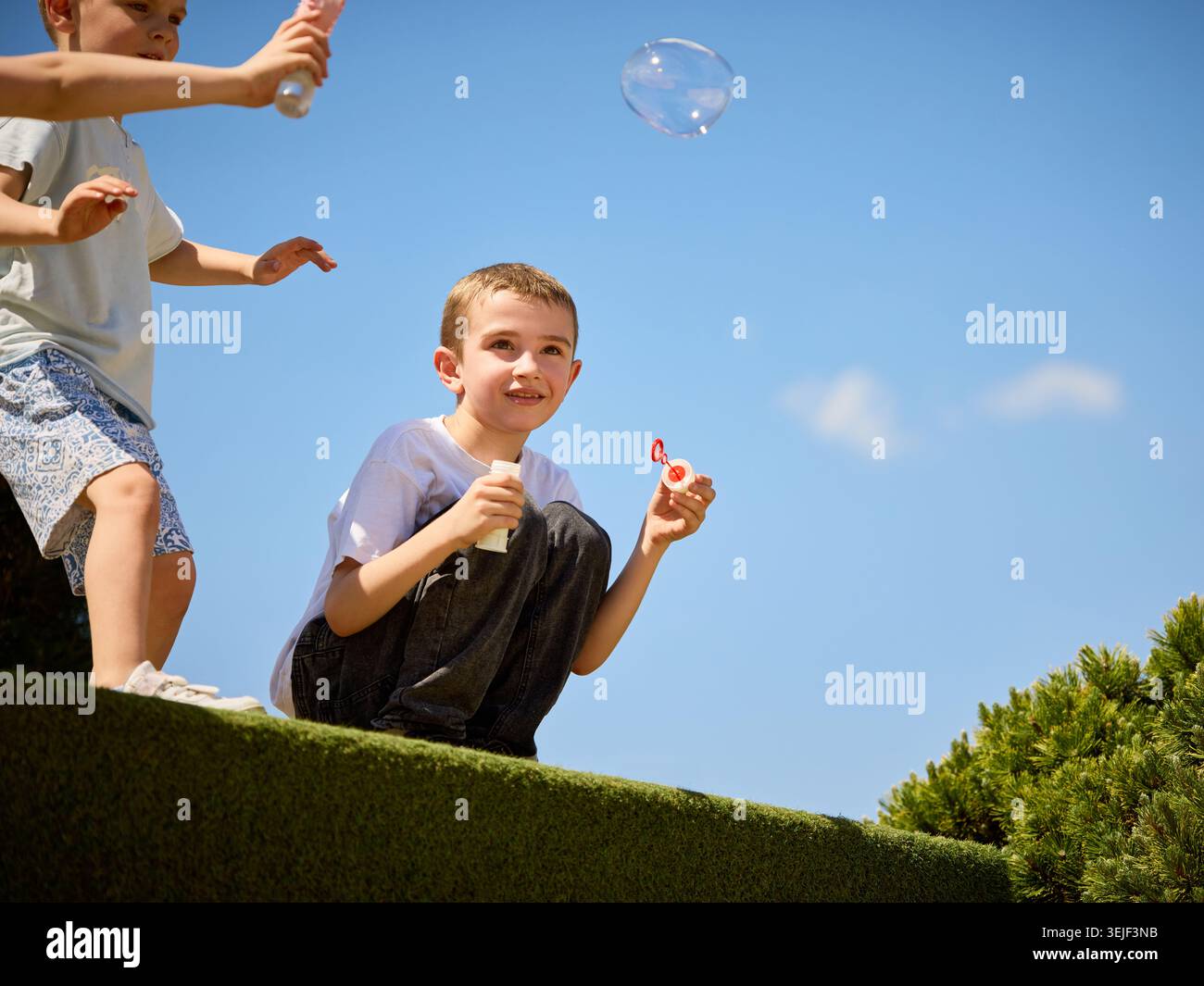 Garçon soufflant des bulles de savon sous le ciel bleu clair dans le parc d'été. Banque D'Images
