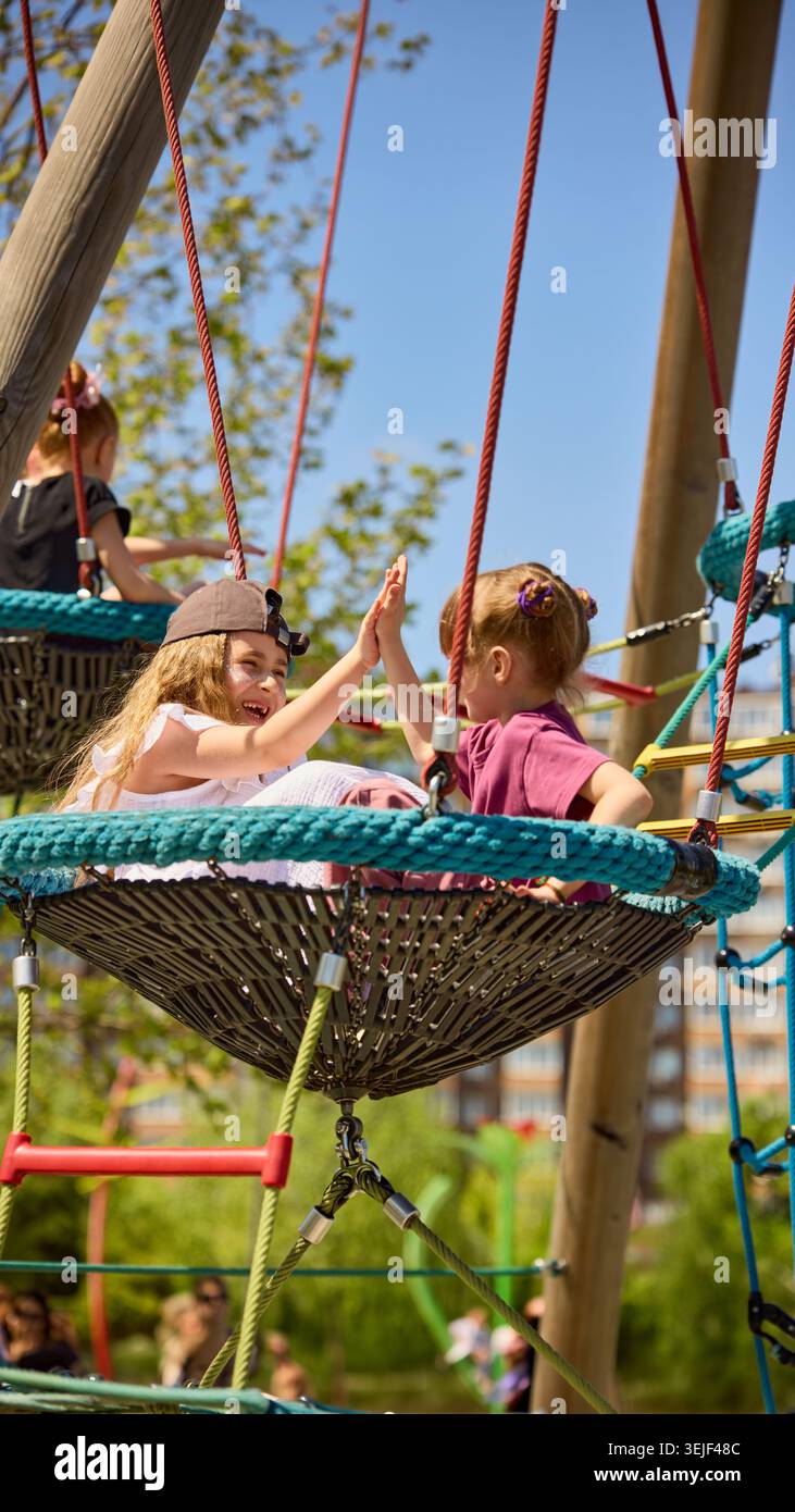 Les filles donnant haut cinq sur le terrain de jeu nid swing dans le parc ensoleillé. Banque D'Images