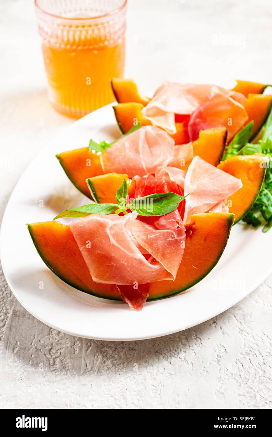 Melon cantaloup au prosciutto et basilic frais, sur une assiette blanche, lumière naturelle, Banque D'Images