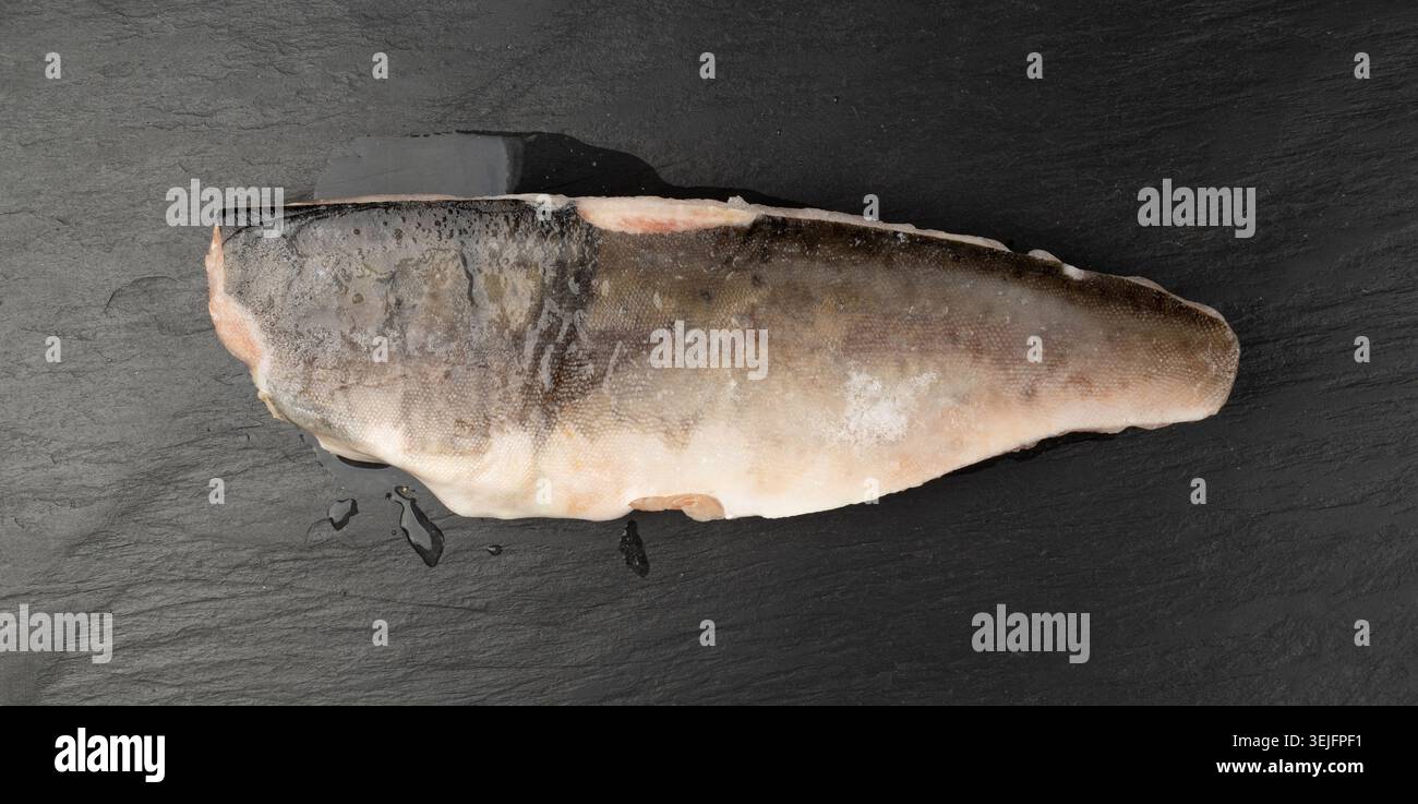 Poisson congelé sur assiette noire, filet de truite rouge, filet de saumon glacé, viande de poisson rouge glacé glacé et peau sur fond foncé vue de dessus Banque D'Images