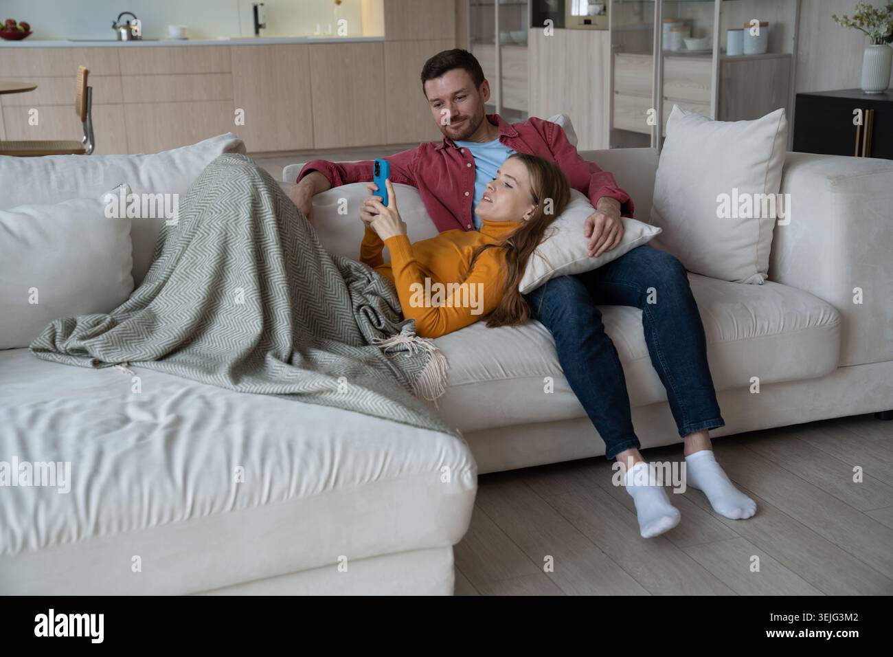 Femme joyeuse couchée sur les genoux de l'homme, tenant un smartphone, souriant tout en ayant videocall avec des parents Banque D'Images