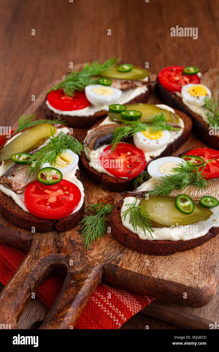 Sandwichs ouverts avec sprats, légumes et herbes, sur une planche de bois, petit déjeuner, collation, Banque D'Images