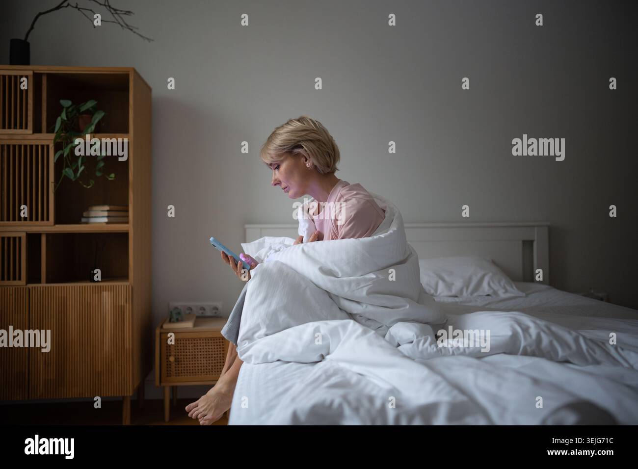 Femme d'âge moyen paresseuse endormie procrastinant au lit avec un smartphone, faisant défiler les flux lisant les nouvelles. Banque D'Images