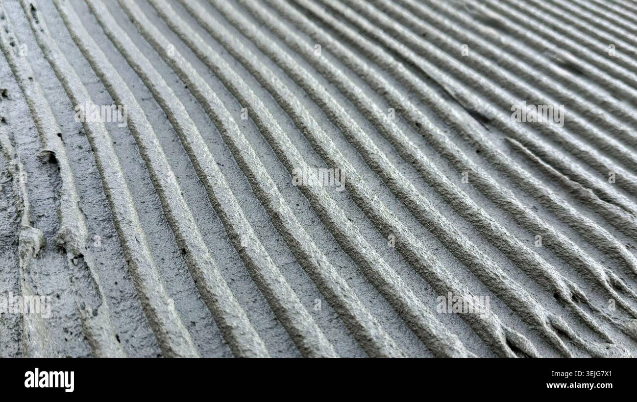 Vue rapprochée du ciment fraîchement appliqué avec des rainures lisses et parallèles sur une surface de construction Banque D'Images
