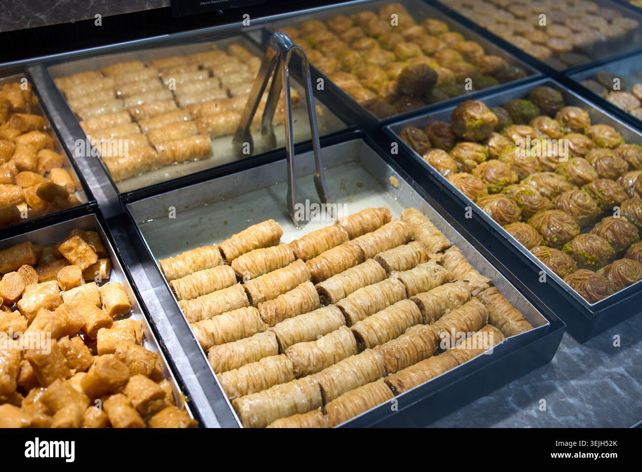 Différents types de baklava traditionnels avec du miel et des pistaches disposés sur des plateaux dans une vitrine de boulangerie. Banque D'Images