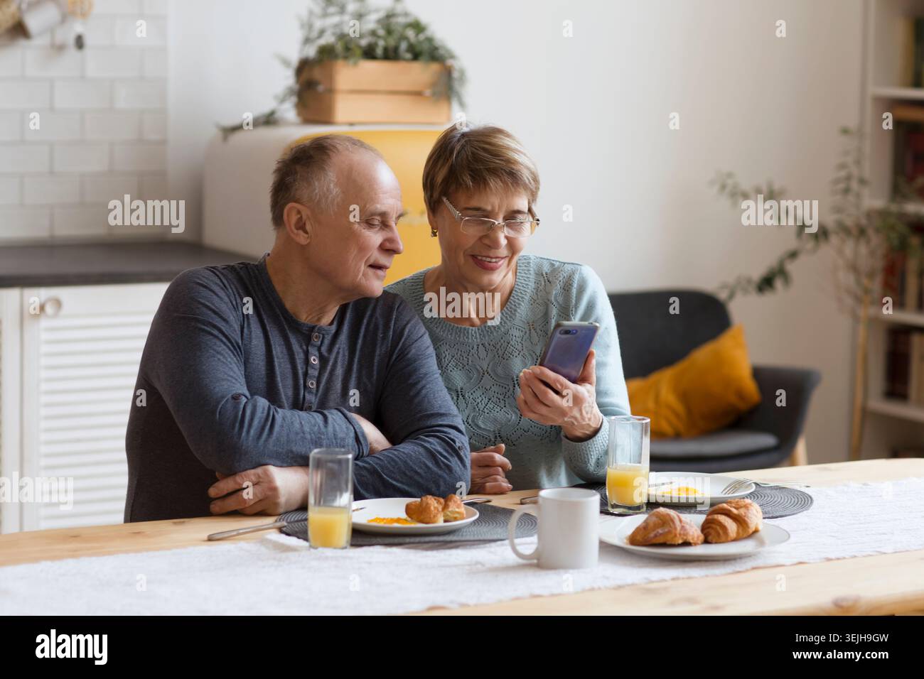 Couple senior prenant le petit déjeuner et utilisant un smartphone à la maison Banque D'Images