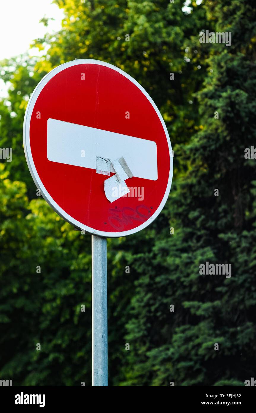 Panneau rouge sans entrée avec autocollants et graffiti sur fond d'arbres verts. Restriction routière et concept de transport. Banque D'Images