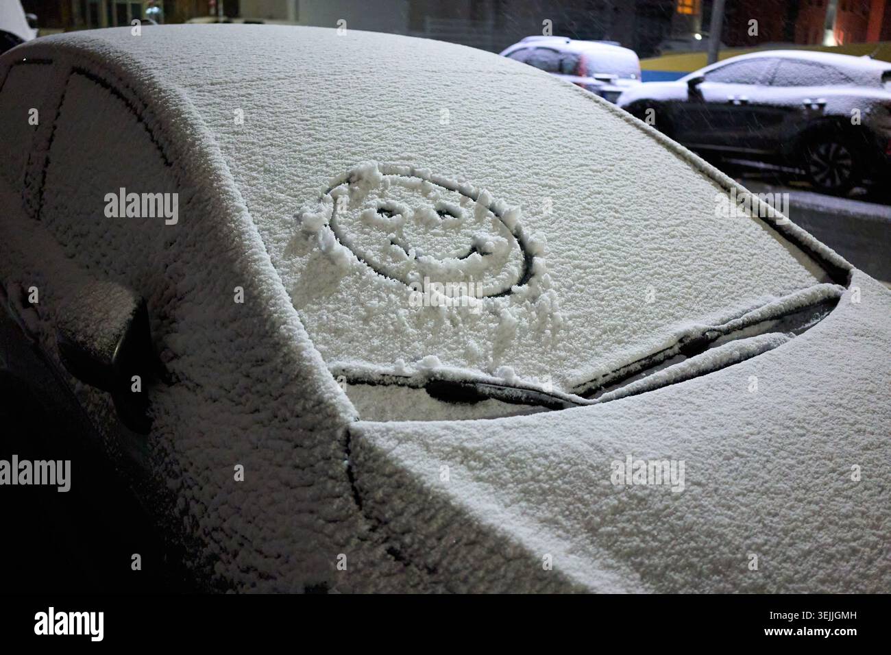 Visage souriant dessiné à la main sur un pare-brise de voiture enneigé garé dans une rue de la ville pendant une froide nuit d'hiver. Banque D'Images