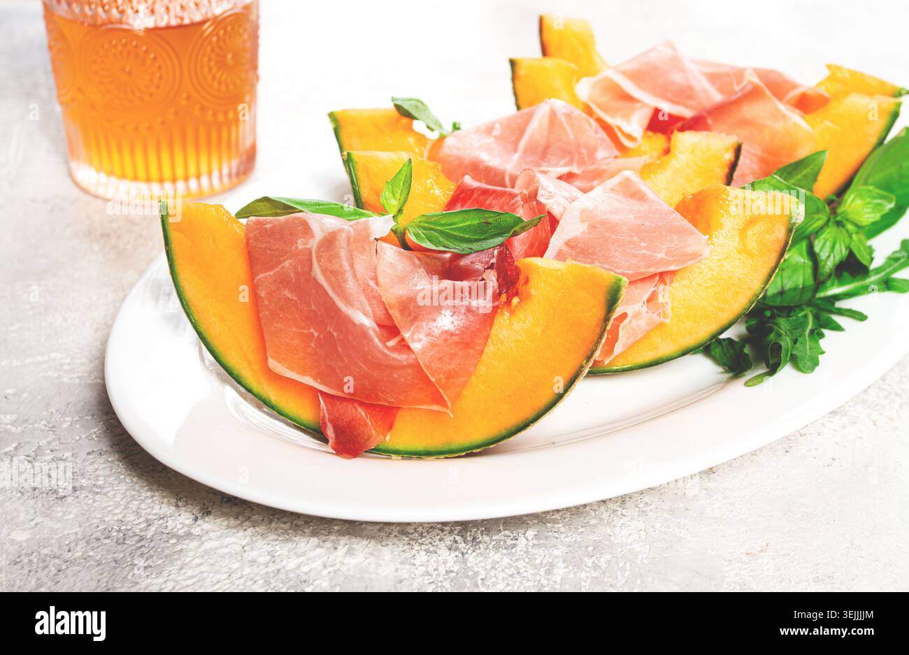 Melon cantaloup au prosciutto et basilic frais, sur une assiette blanche, lumière naturelle, Banque D'Images