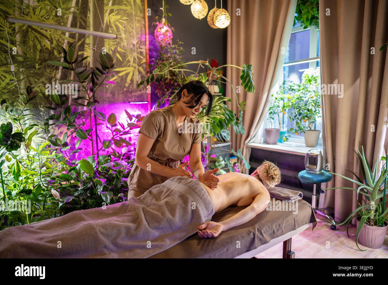 Femme allongée sur la table obtenant un massage corporel de dame professionnelle cosmétologue sur la région du bas du dos. Banque D'Images