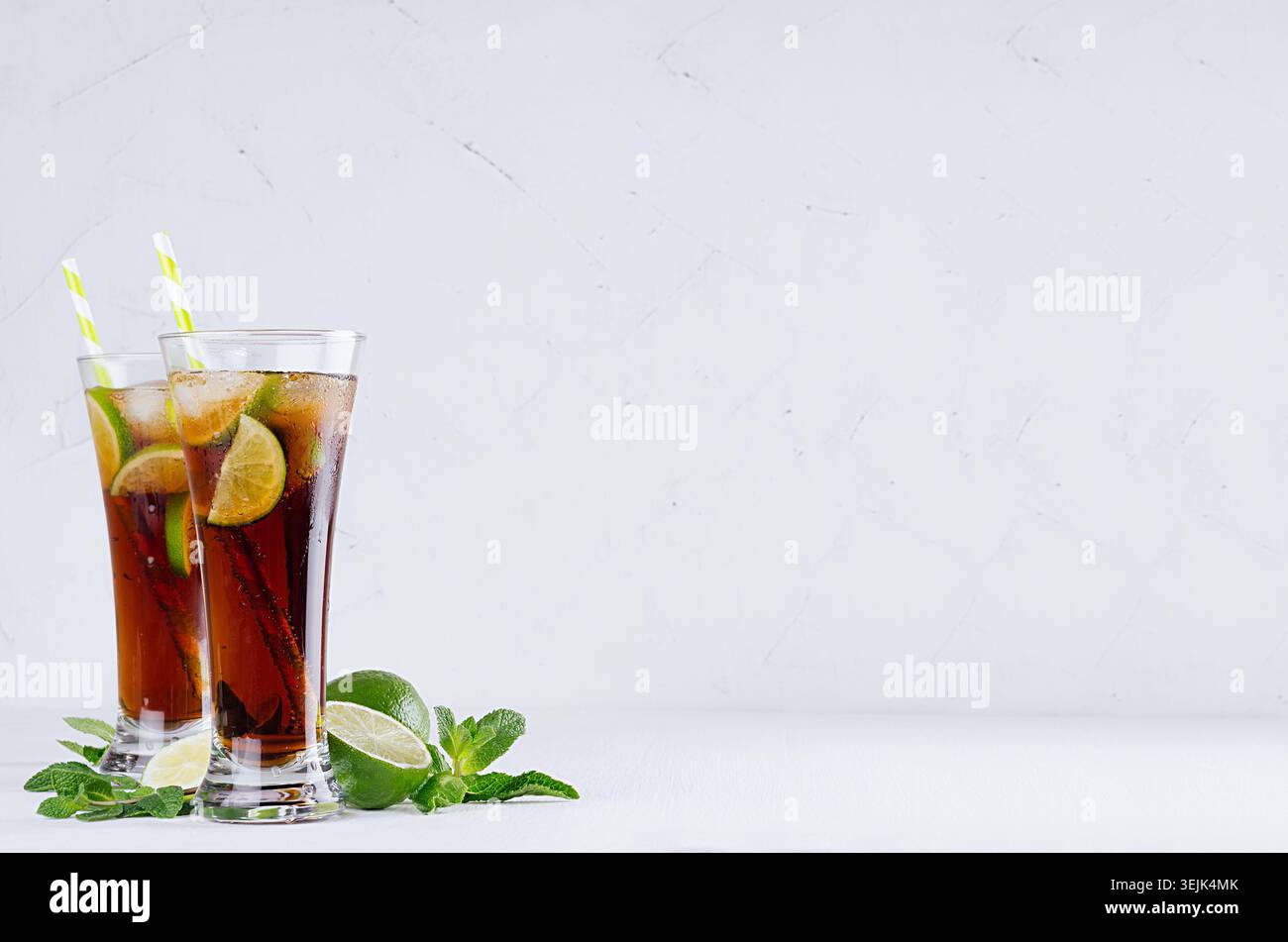 Cocktail rafraîchissant d'été pétillant de cola, glace, citron vert, feuille de menthe sur fond blanc doux avec espace de copie. Banque D'Images