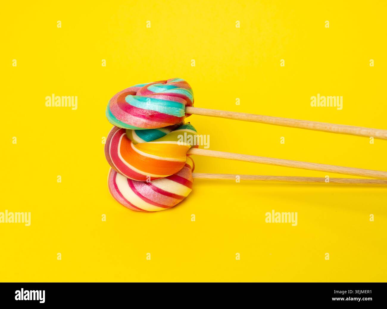 Sucette de couleur, bonbons spiralés sur bâton, sucette rayée colorée, caramel aux fruits ronds, confiserie multicolore, sucette circulaire sur fond jaune Banque D'Images