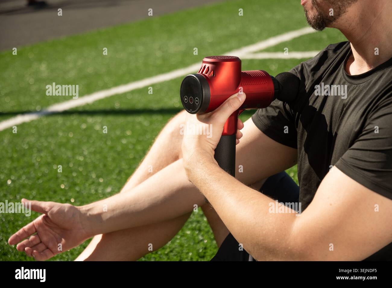 Homme massant le corps et la main avec dispositif de percussion de massage après l'entraînement. Banque D'Images