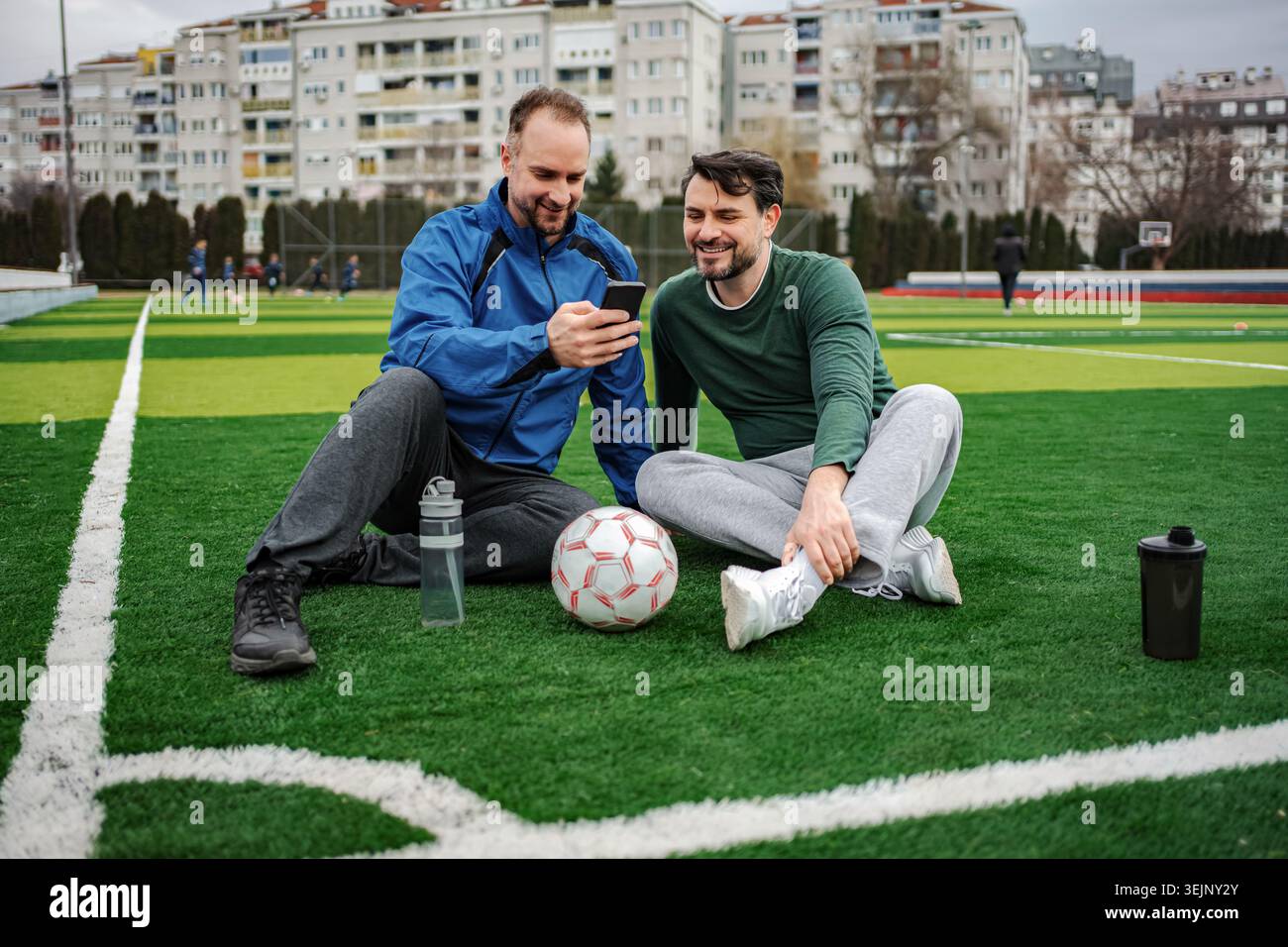 Amis se reposant sur le terrain de football regardant smartphone Banque D'Images