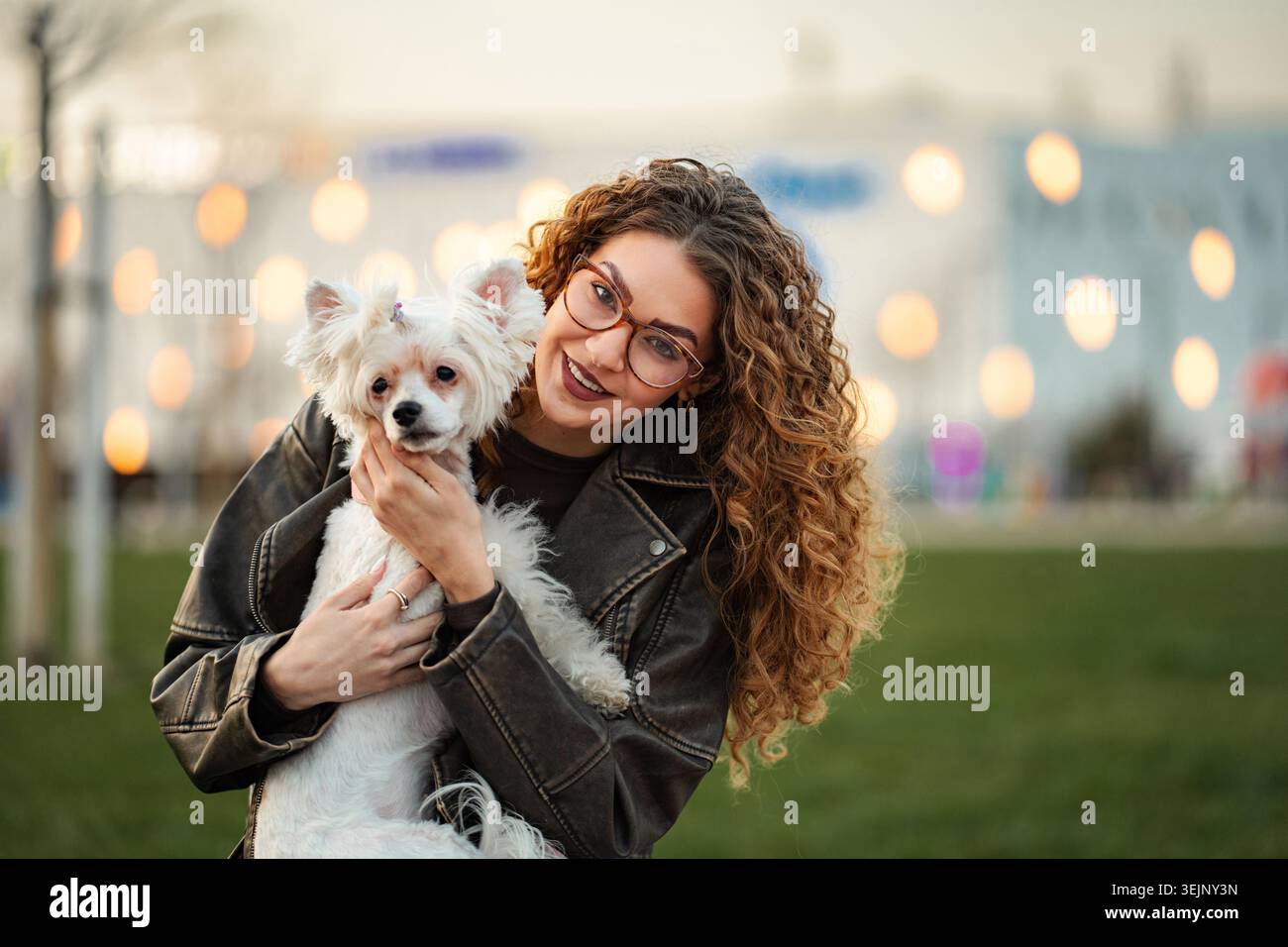 Femme souriant tout en tenant son chien blanc dehors Banque D'Images