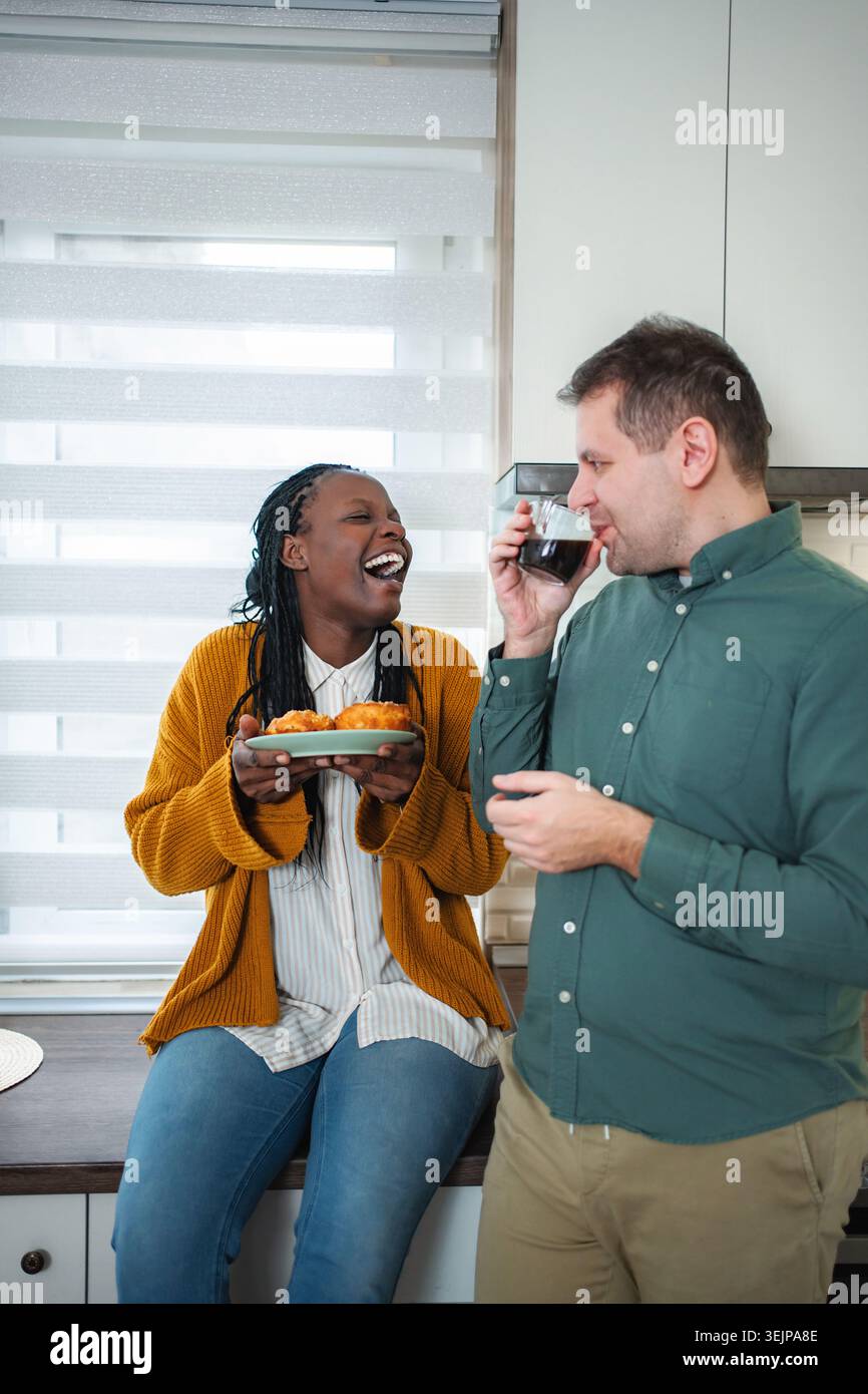 Heureux couple multiracial appréciant le café et les pâtisseries dans la cuisine Banque D'Images