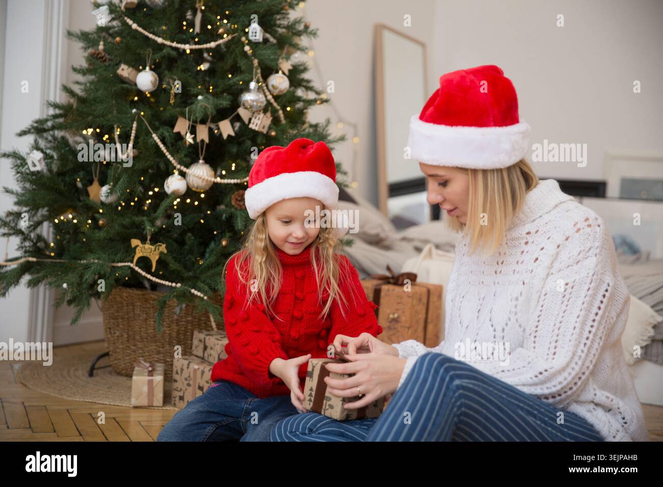 Maman et fille enfant dans un chapeau Santas avec des cadeaux de Noël à la maison près de l'arbre de Noël. La famille rencontre Noël ensemble Banque D'Images
