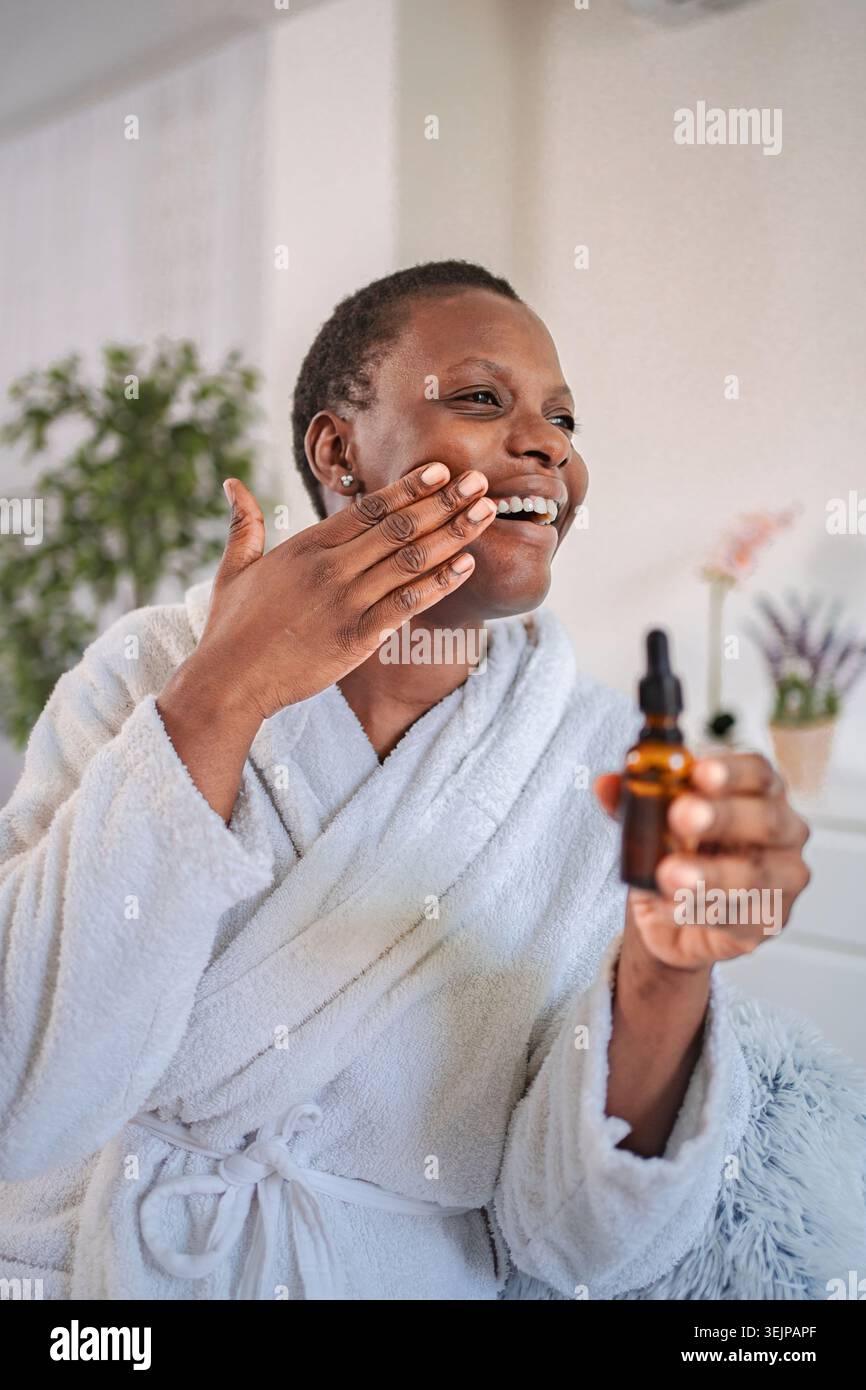 Femme souriante appliquant le sérum sur le visage pour la routine de soins de la peau Banque D'Images