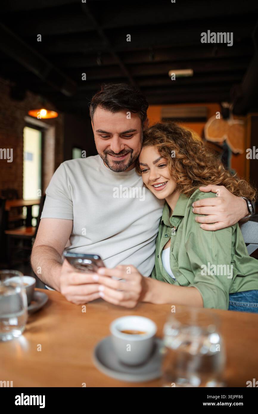 Couple regardant smartphone et souriant dans le café Banque D'Images