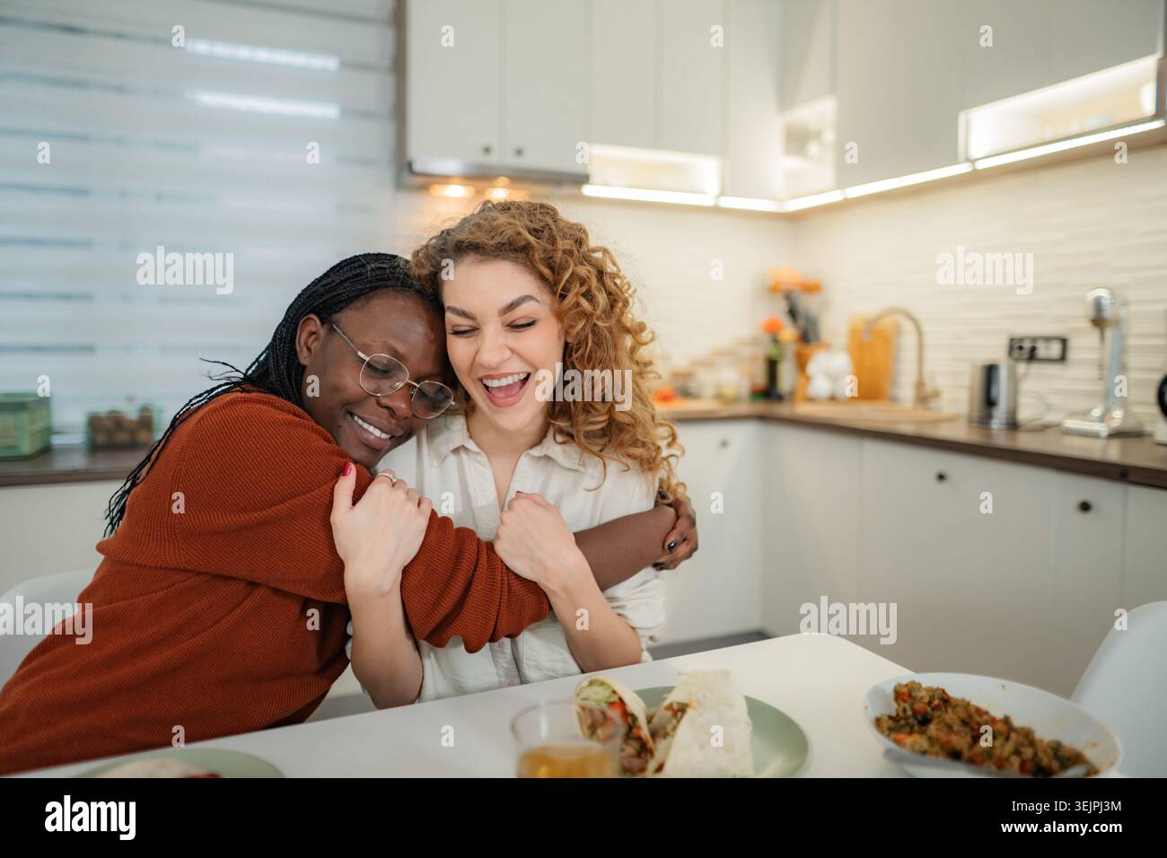 Amies embrassant rire ensemble dans la cuisine Banque D'Images