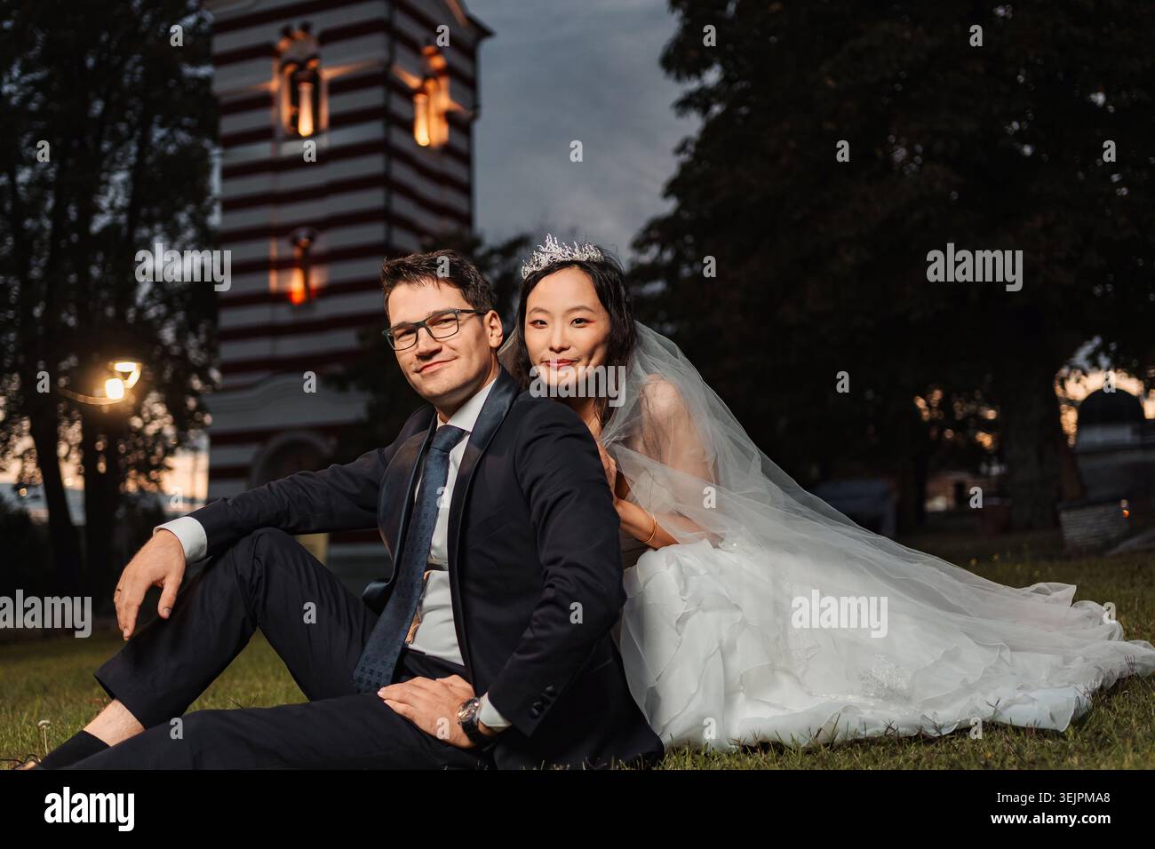 Couple de mariage interracial assis sur l'herbe au crépuscule Banque D'Images