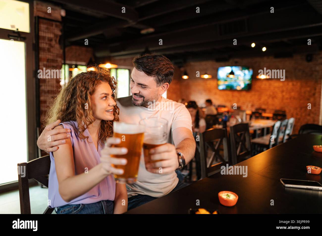 Couple buvant de la bière et mangeant des collations au comptoir dans un pub Banque D'Images