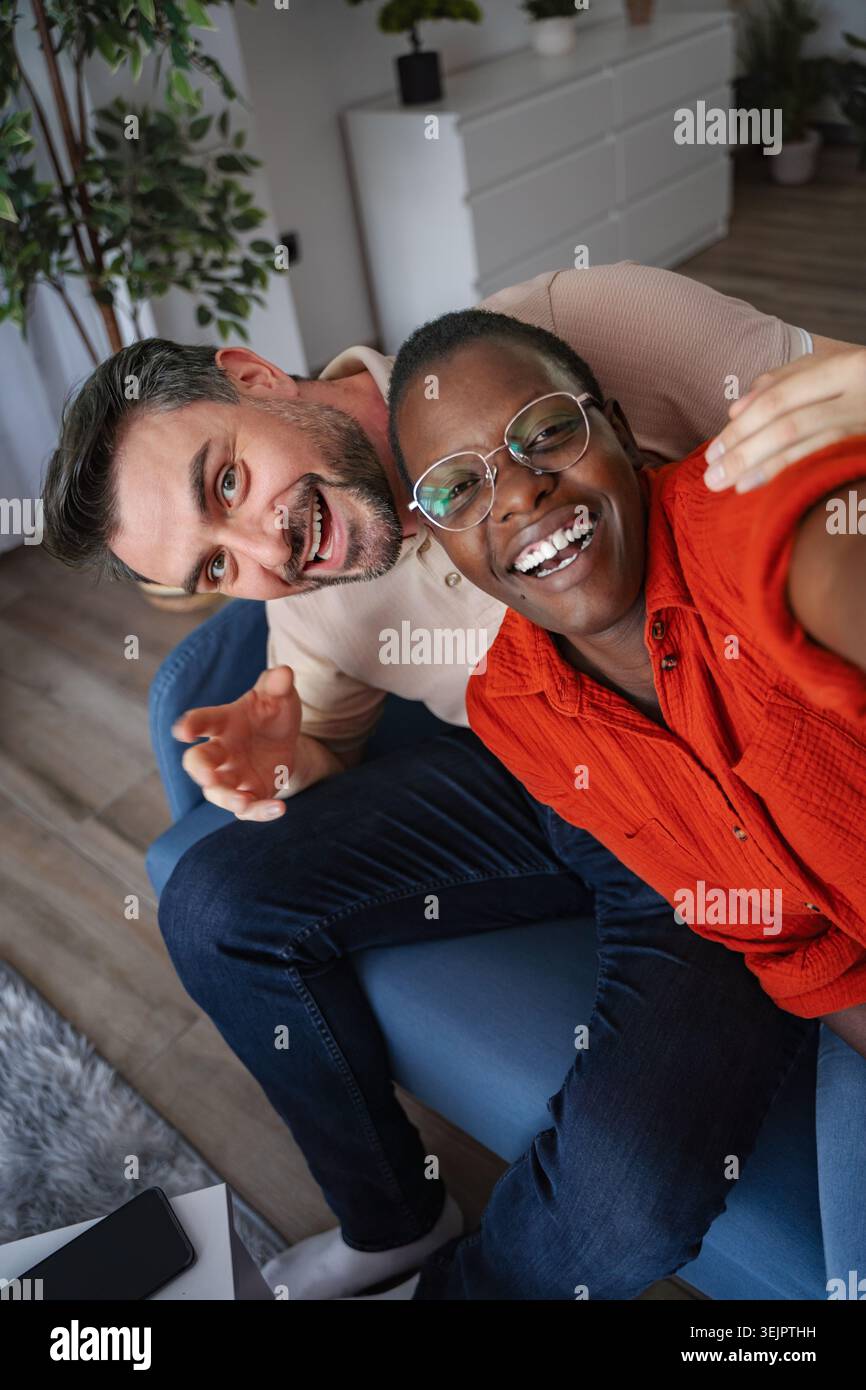 Couple heureux prenant un selfie tout en étant assis sur le canapé à la maison Banque D'Images