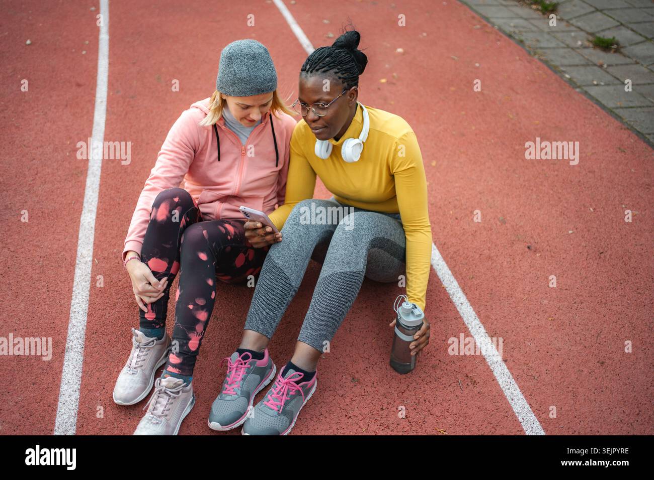 Amies féminines se relaxant sur la piste en regardant le téléphone Banque D'Images