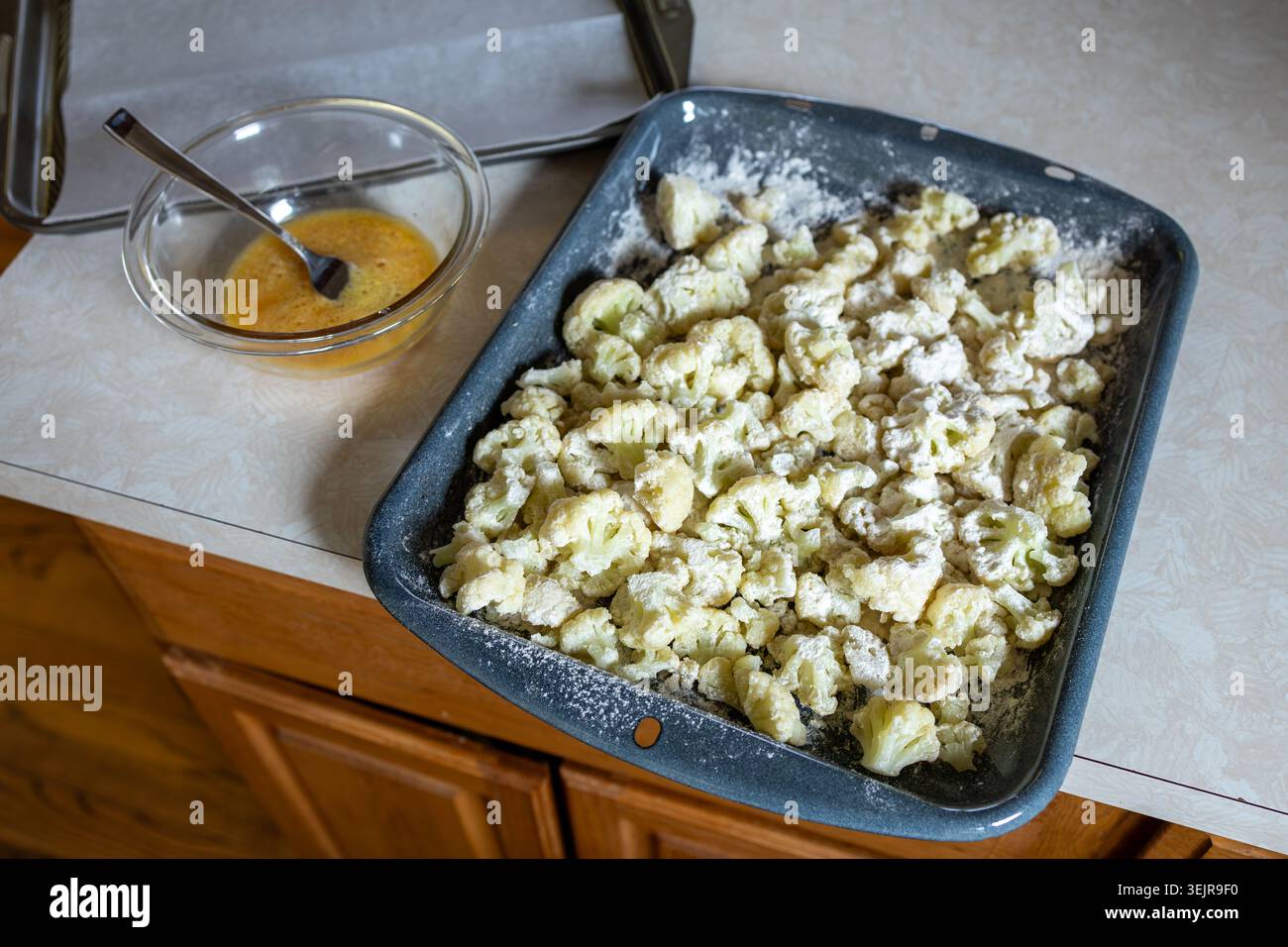Les morceaux de chou-fleur sont enrobés de farine sur un comptoir. Un bol avec un mélange se trouve à côté du plateau. Cette scène représente la préparation des aliments pour la cuisson. Banque D'Images