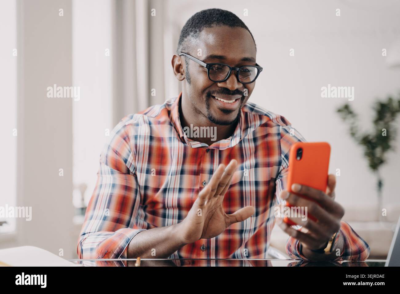 Joyeux homme noir faisant appel vidéo sur smartphone à la maison et saluant Bonjour Banque D'Images