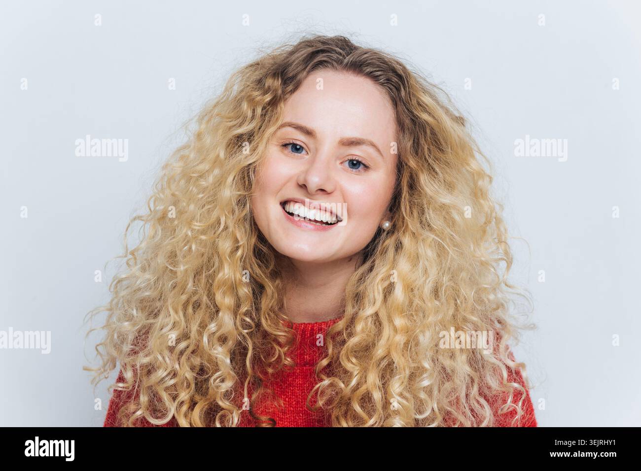 Jeune femme souriante avec des cheveux blonds bouclés pose pour un portrait de studio propre Banque D'Images
