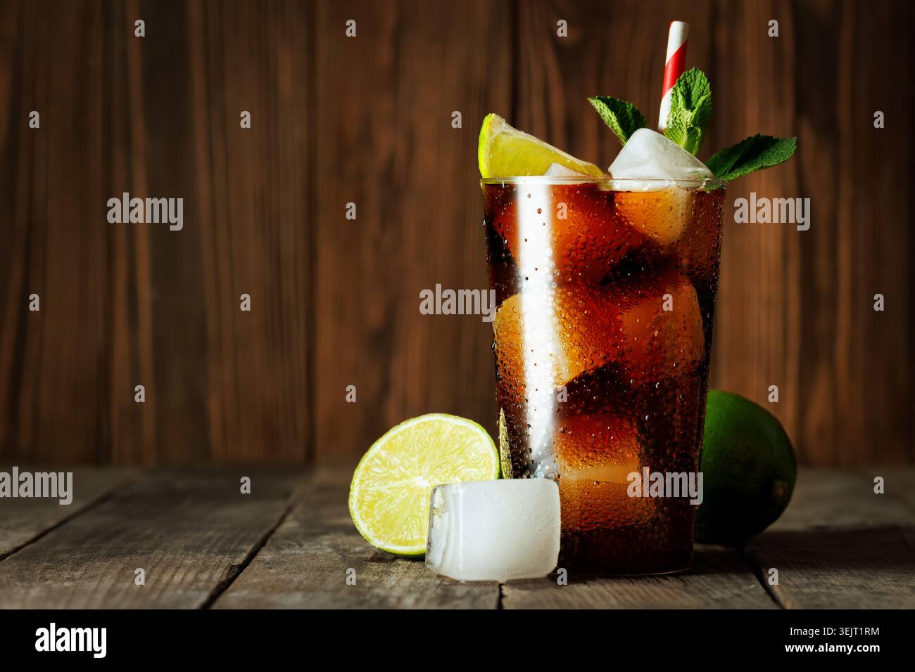 Cuba libre cocktail pétillant cola et rhum est froid dans le verre avec de la glace, des tranches de citron vert et de la menthe fraîche sur la surface en bois Banque D'Images