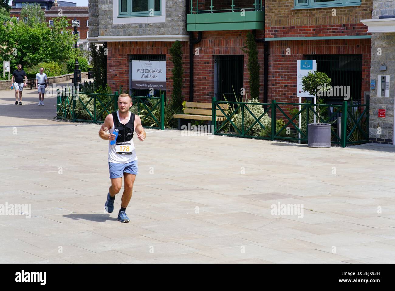 Coureur masculin avec numéro de dossard en compétition sur la place pavée ensoleillée pendant la course de course à pied de Tonbridge avec des bâtiments historiques en arrière-plan.Tonbridge, Kent Banque D'Images