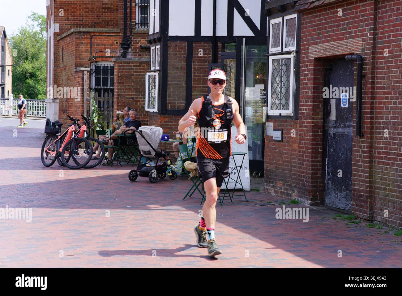 Coureur masculin avec bavoir 165 en compétition sur la rue pavée ensoleillée pendant la course de course à pied de Tonbridge avec des bâtiments historiques en arrière-plan.Tonbridge, Kent Banque D'Images