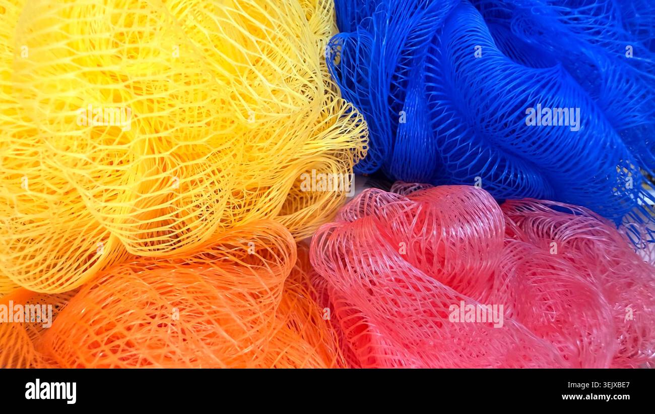 Éponges colorées en maille de bain en gros plan, fond texturé lumineux des accessoires de nettoyage. Banque D'Images