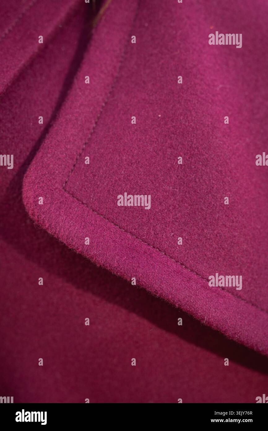 L'image montre une texture macro en gros plan d'une poche ou d'un revers de manteau en laine violette ou magenta éclatante avec des coutures soignées. Banque D'Images