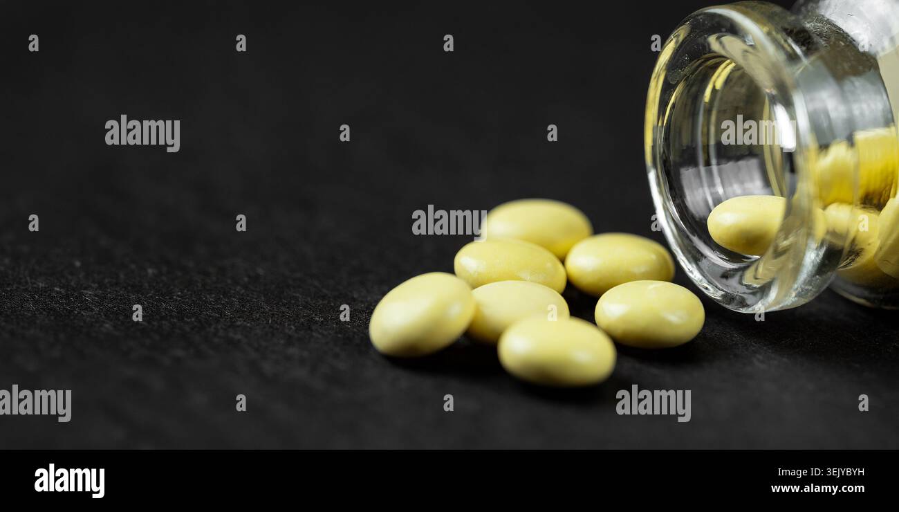 Comprimés ronds de médicaments jaunes débordant d’un petit flacon en verre sur une surface sombre Banque D'Images