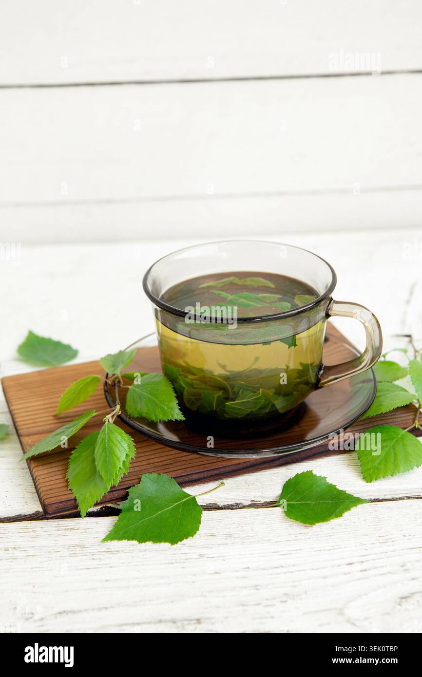 Thé de feuilles de bouleau, Betula servi dans une tasse en verre clair sur un fond de planche de bois blanc, avec des feuilles de bouleau fraîches et des branches pour la décoration. Banque D'Images