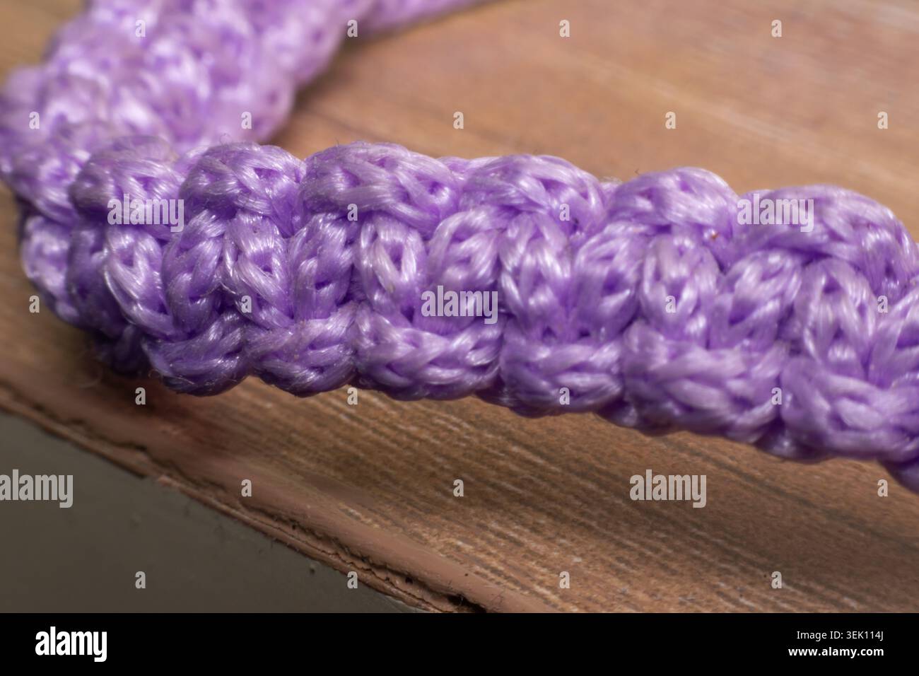 Gros plan d'une corde tressée violette présentant la durabilité de l'artisanat de texture de fibre tissée et le motif détaillé sur une surface en bois Banque D'Images