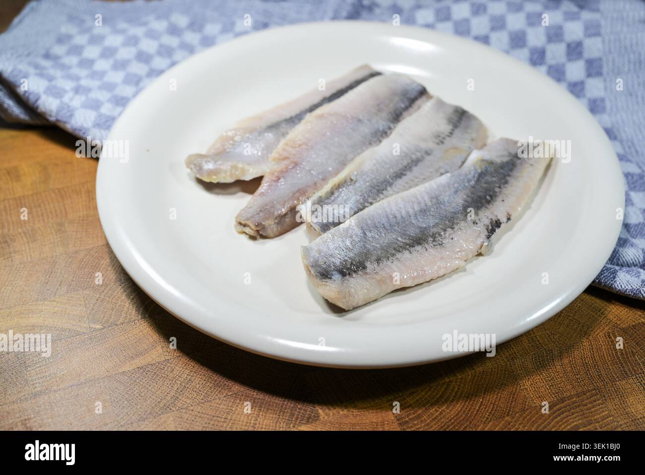 Filets de hareng soudés (maatjes en néerlandais) sur une assiette, harengs immatures au sel doux, ingrédient pour divers plats de poisson, serviette de cuisine bleue sur une table en bois, foyer sélectionné, profondeur de champ étroite Banque D'Images
