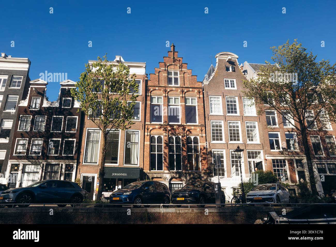 Amsterdam, pays-Bas - 18 avril 2026 : rangée de maisons de canal hollandaises traditionnelles avec façades à pignons historiques le long d'un canal dans le centre d'Amsterdam sous c Banque D'Images