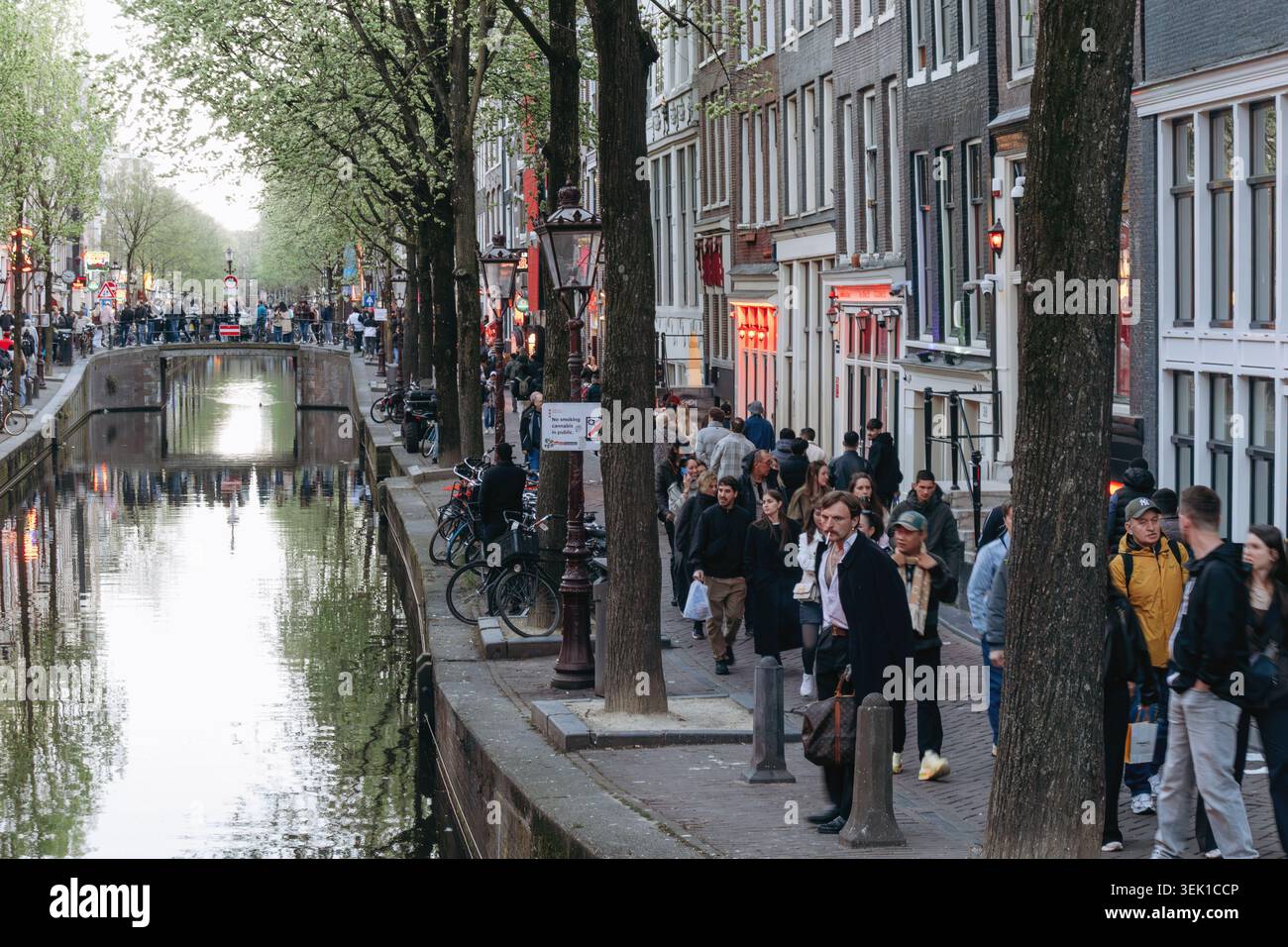 Amsterdam, pays-Bas - 18 avril 2026 : vue en soirée sur le quartier rouge d'Amsterdam le long d'un canal historique avec des fenêtres rouges illuminées, groupe animé Banque D'Images